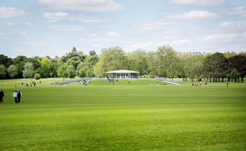 An external photo of the cafe in the park with people sitting on the banks