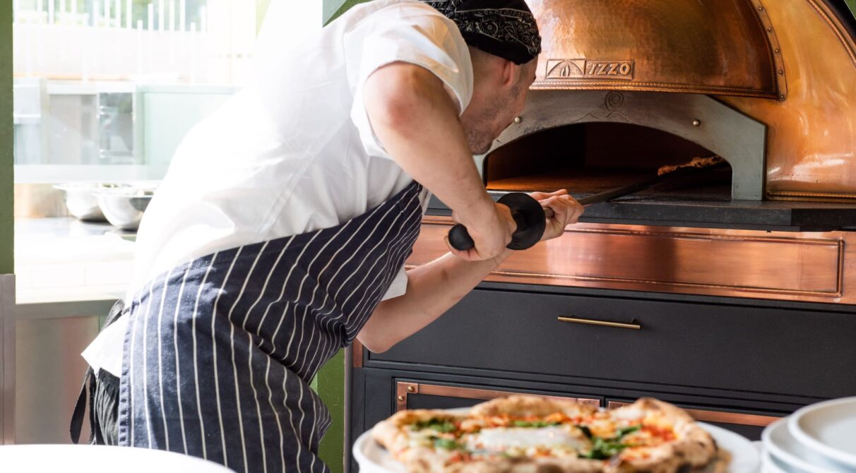 A chef putting in pizza into a pizza oven